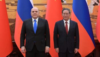 Mijaíl Mishustin y Li Qiang de pie, uno junto al otro, ante banderas de Rusia y China