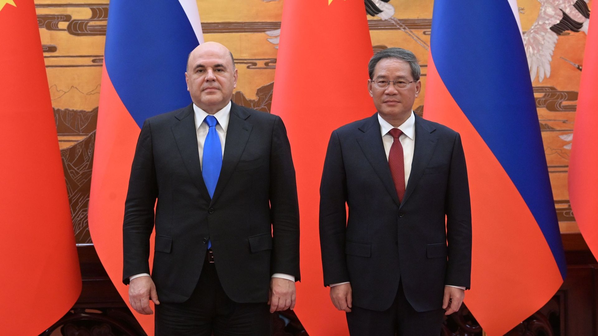 Mijaíl Mishustin y Li Qiang de pie, uno junto al otro, ante banderas de Rusia y China
