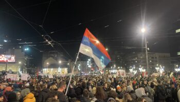 Miles de personas con una bandera serbia en la plaza Slavija de Belgrado, de noche, durante la protesta del 22 de diciembre de 2024