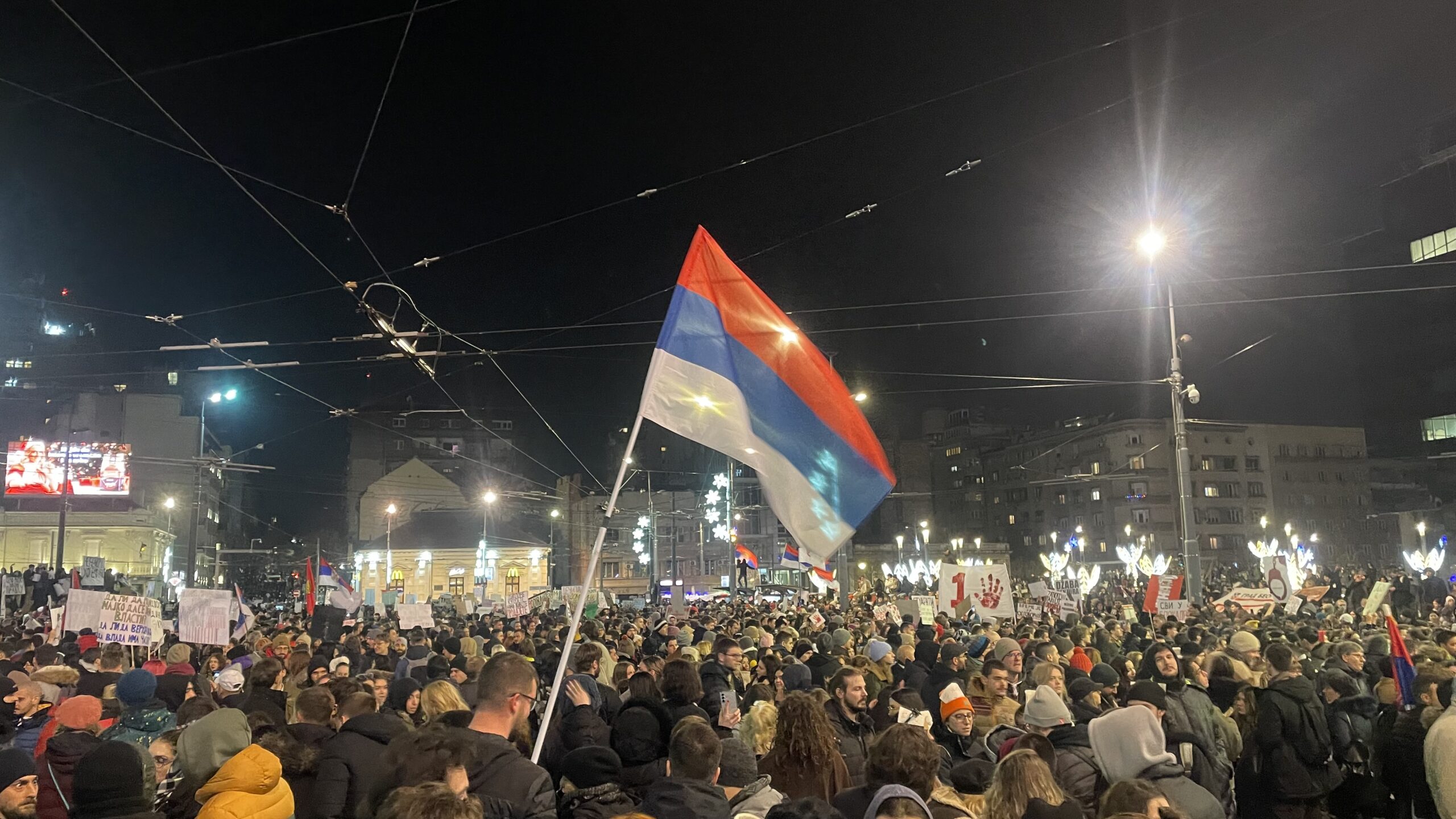 Miles de personas con una bandera serbia en la plaza Slavija de Belgrado, de noche, durante la protesta del 22 de diciembre de 2024